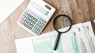 Formul&aacute;rios fiscais, calculadora e lupa sobre uma secret&aacute;ria